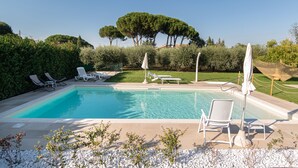 A rectangular swimming pool with clear blue water, surrounded by white lounge chairs and umbrellas, with a backdrop of neatly trimmed hedges and a large tree. - Rosa di Assisi (Bastia Umbra)