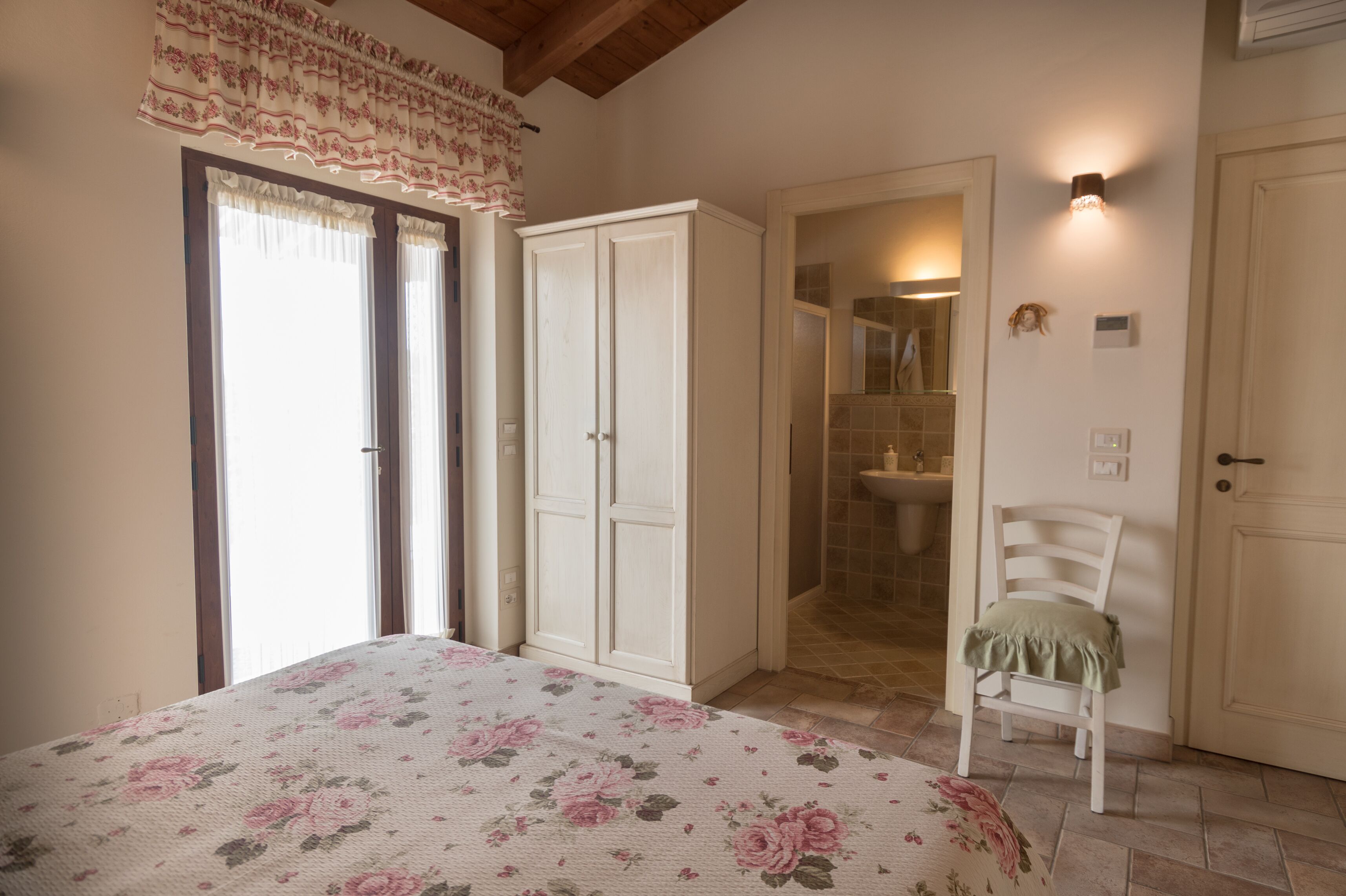 A bedroom with a bed, a wardrobe, a chair, and a bathroom visible through an open door.