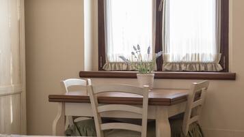 Un coin repas avec une table en bois et deux chaises blanches, un pot de lavande posé sur le rebord de la fenêtre et des rideaux légers aux fenêtres.