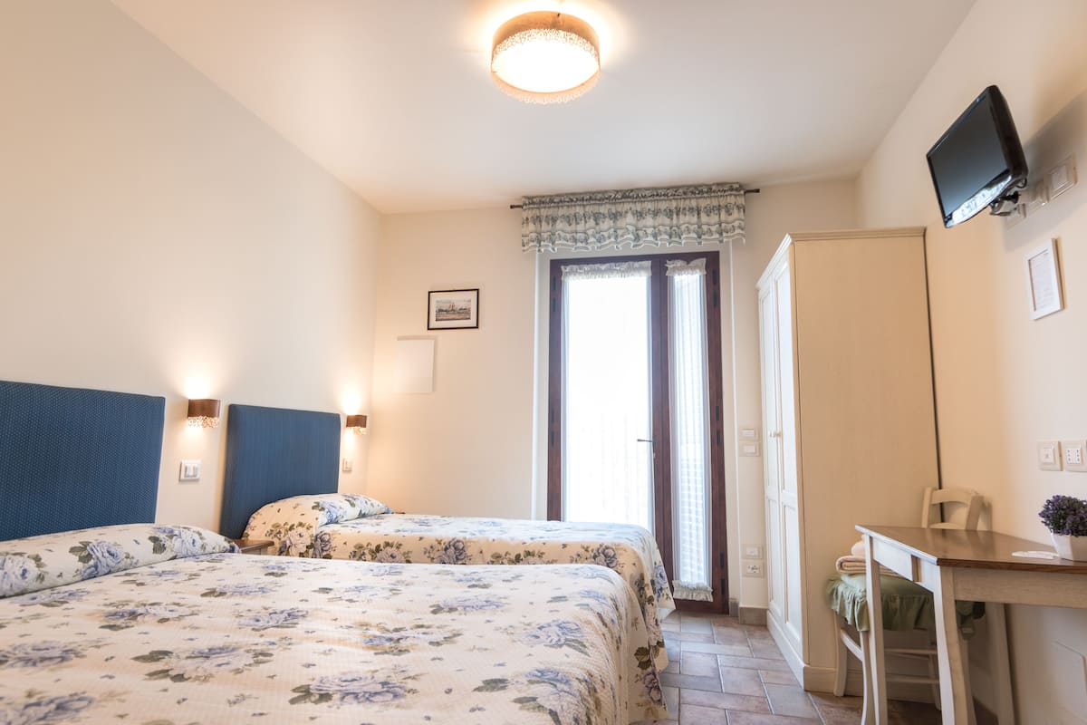 A bedroom with two beds, a desk, a chair, a television, and a window with curtains.