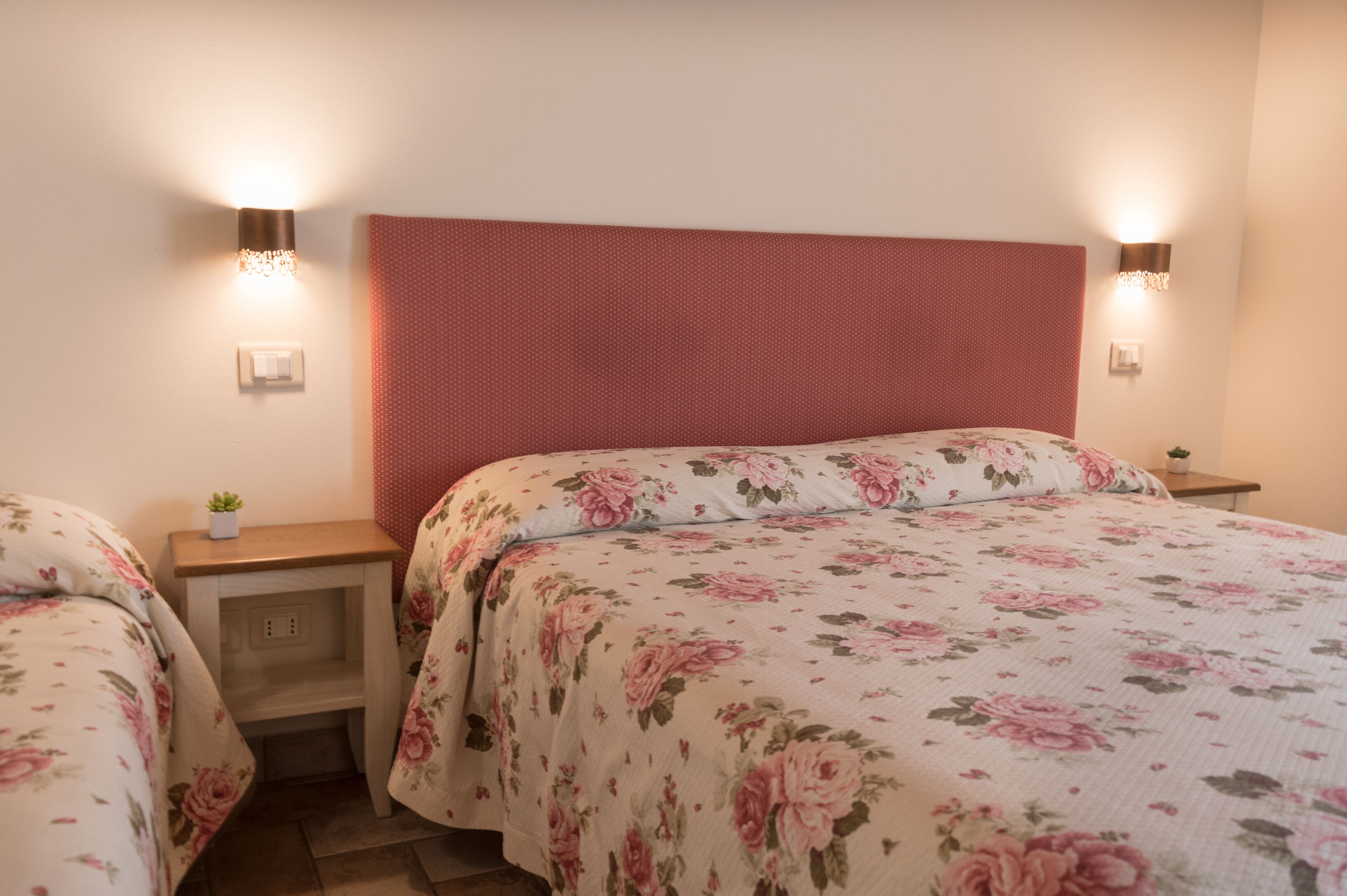 Quarto com uma cama grande, duas mesas de cabeceira, um criado-mudo e um candeeiro fixado na parede.