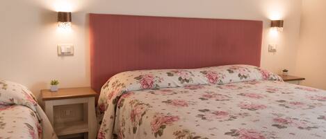Quarto com uma cama grande, duas mesas de cabeceira, um criado-mudo e um candeeiro fixado na parede.