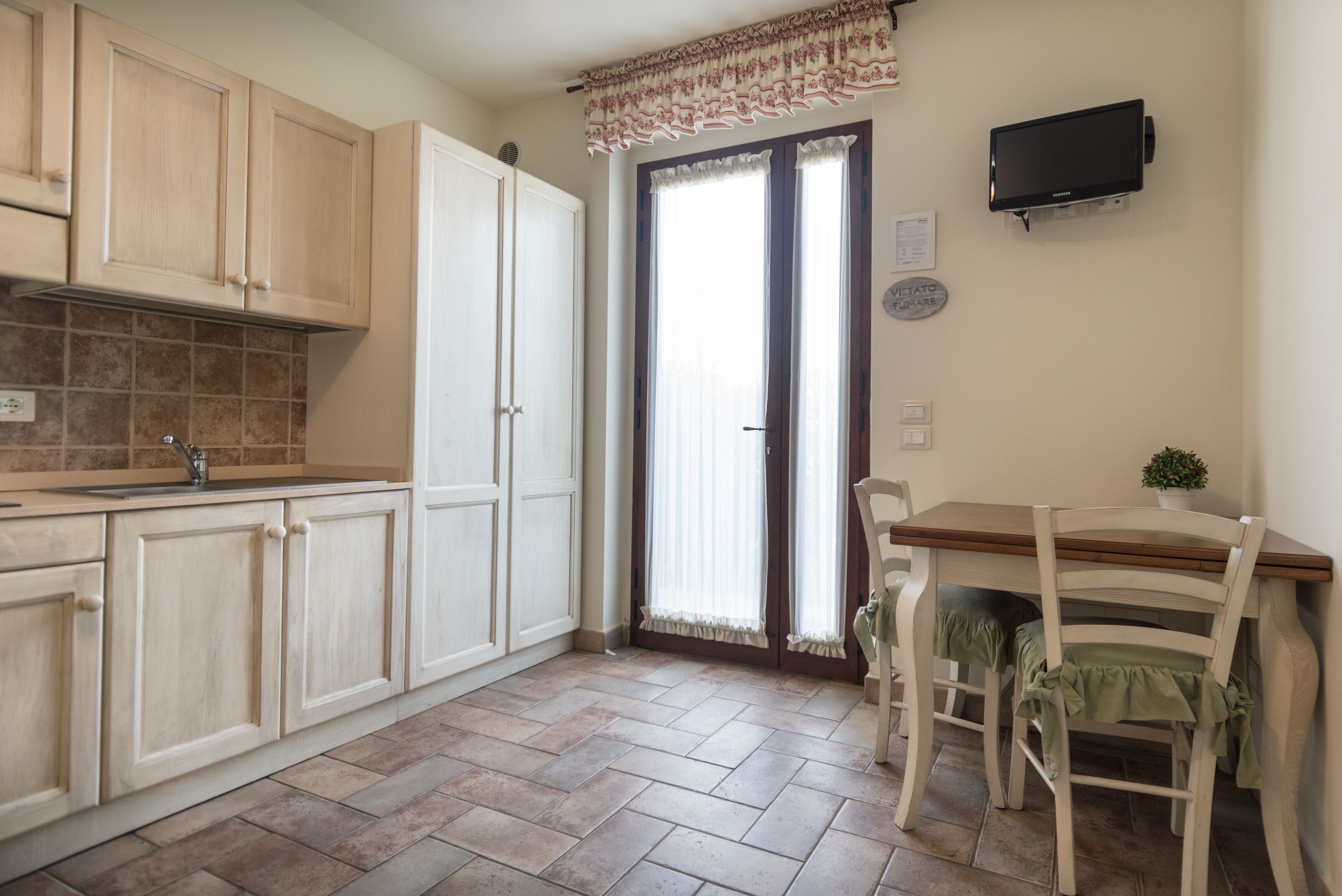 A kitchen with wooden cabinets, a tiled backsplash, a dining table with chairs, and a television mounted on the wall.