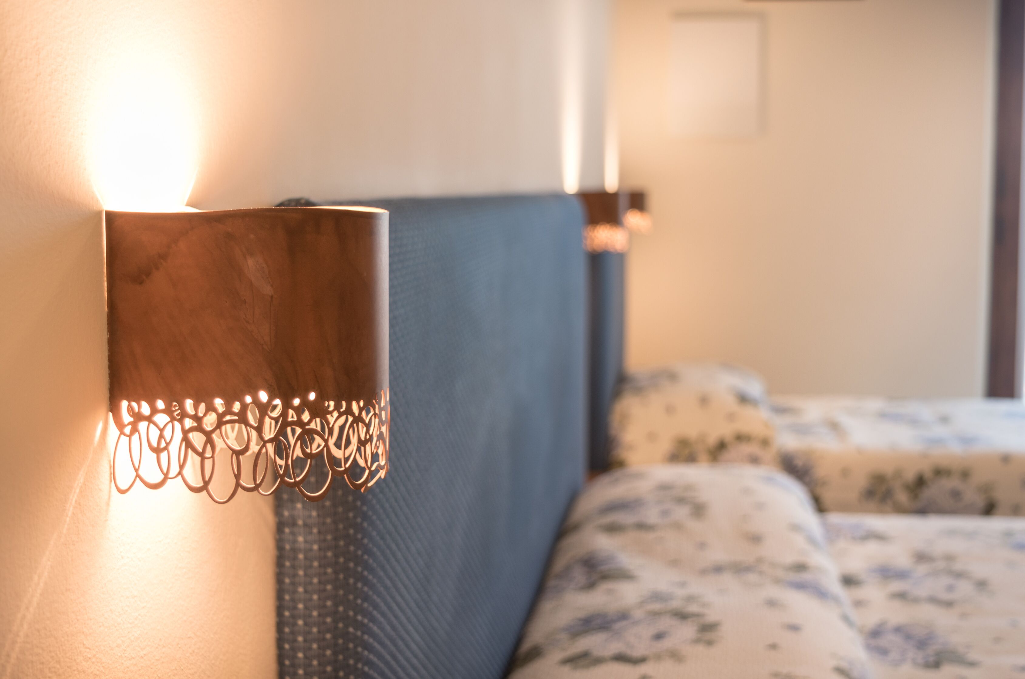 Cama com cabeceira e luminária fixada na parede.