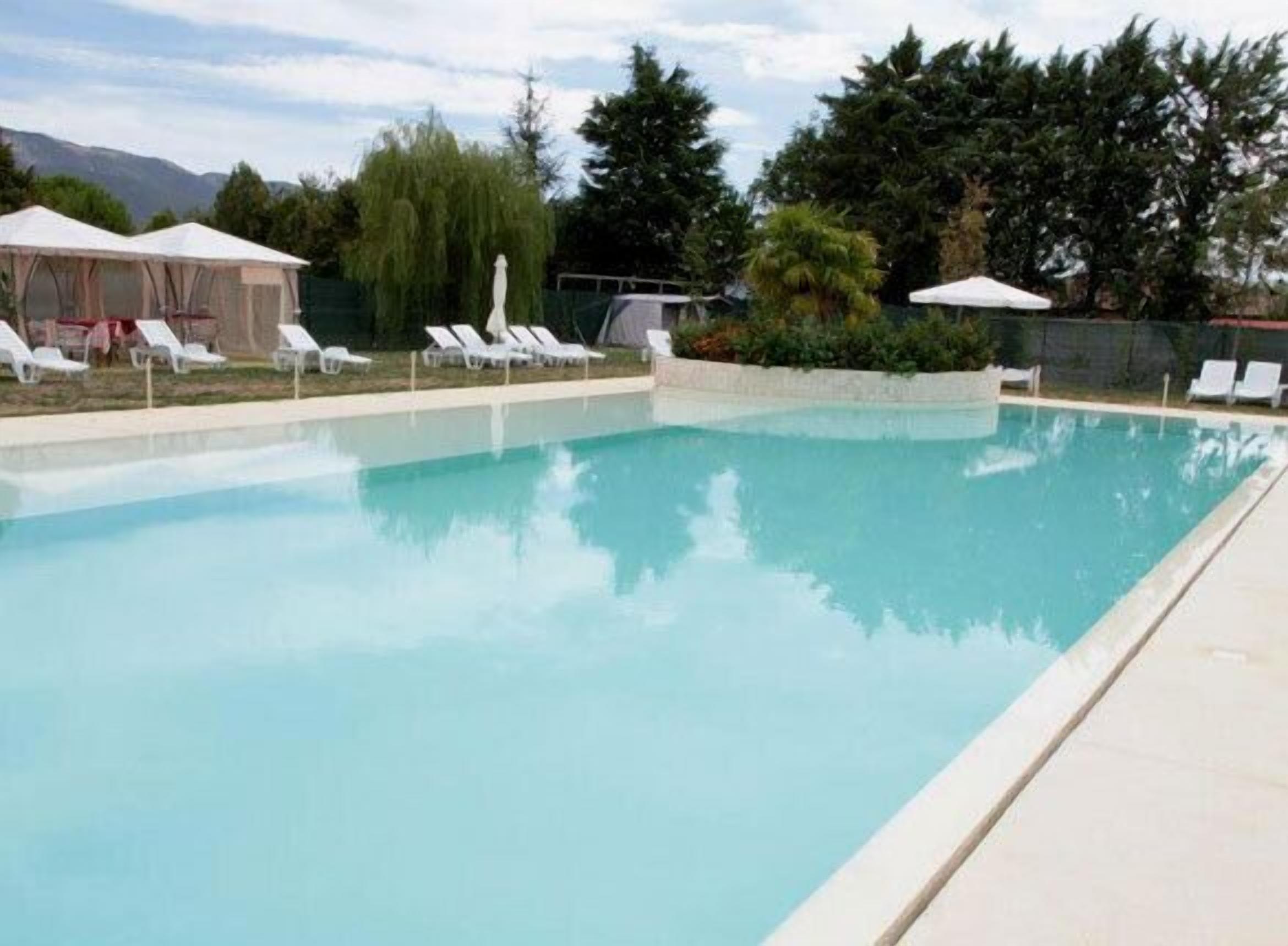 A swimming pool with white lounge chairs and umbrellas.