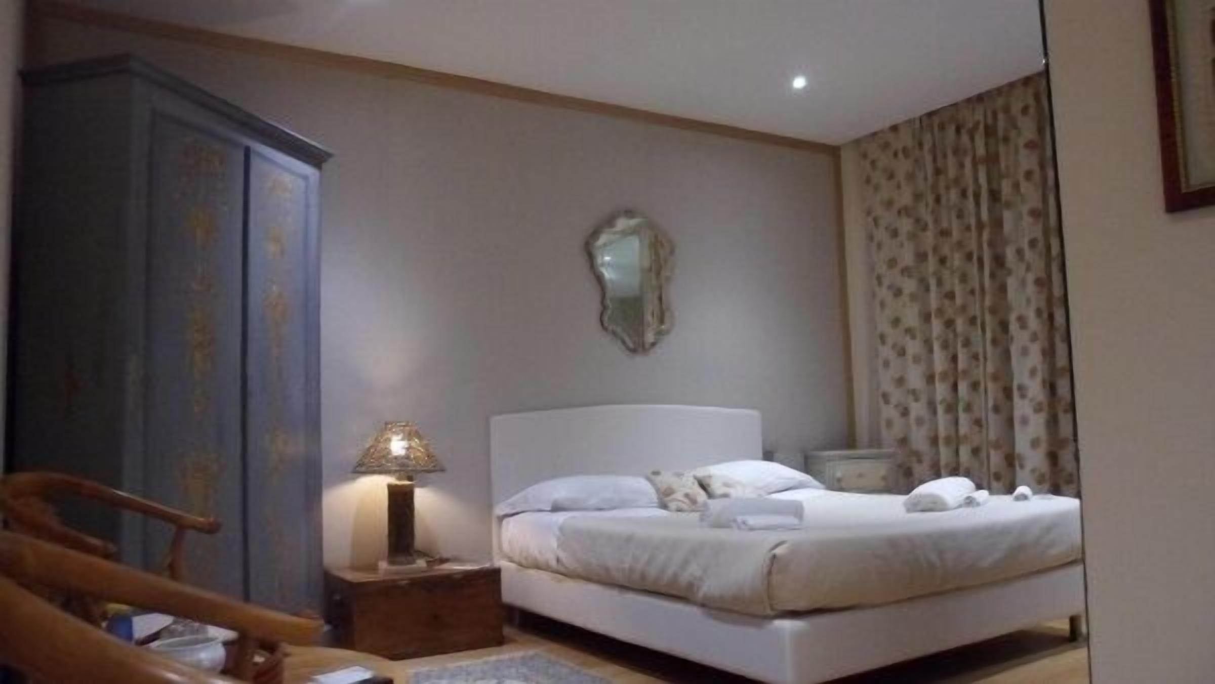 Une chambre à coucher avec un lit, une table de chevet, une lampe, une armoire et un miroir au mur.