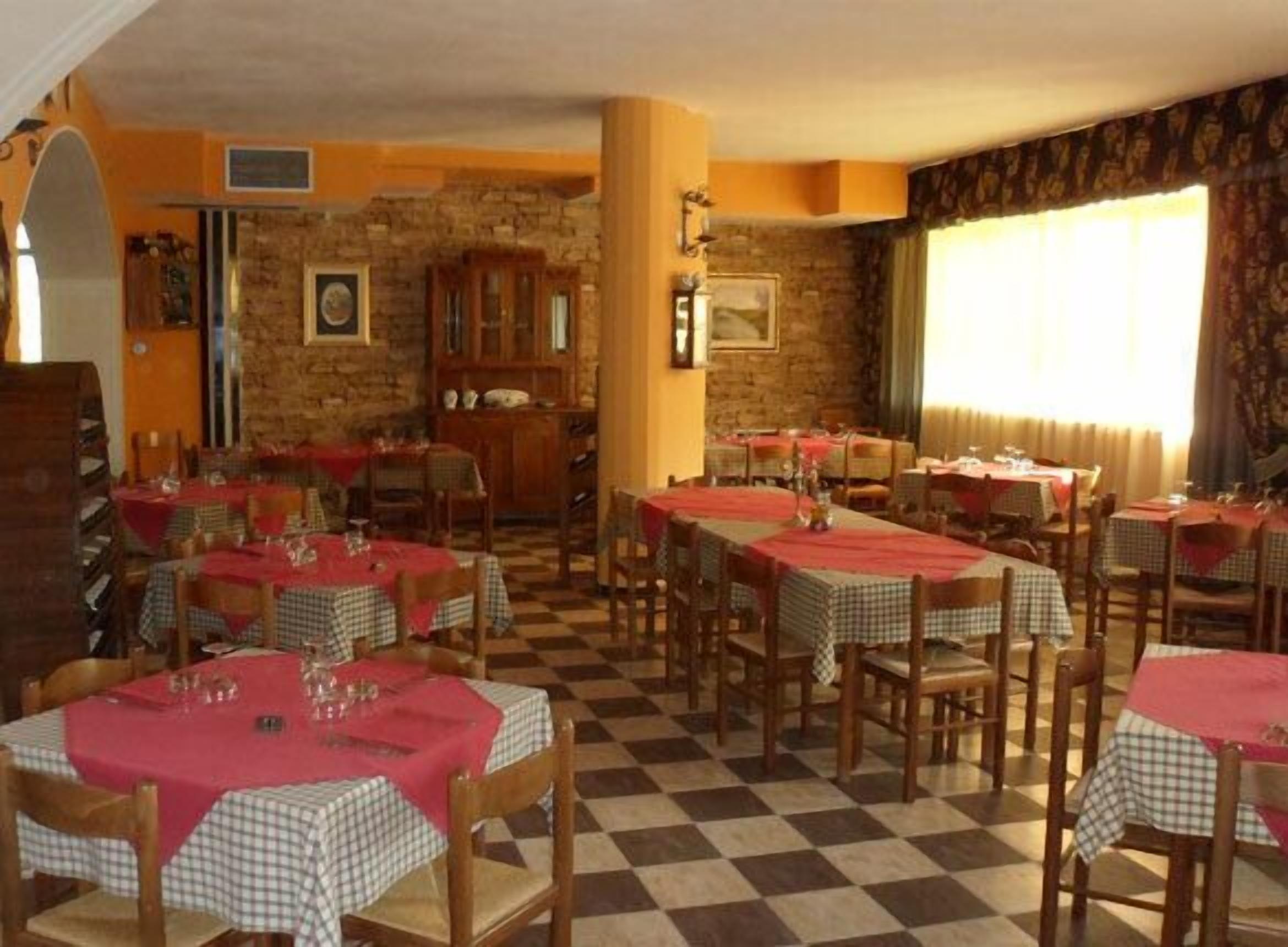 A restaurant with checkered tablecloths, wooden chairs, and a stone wall. Tables are set with glasses and cutlery.
