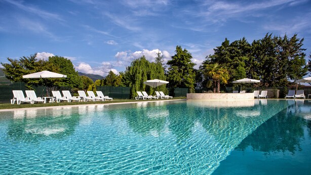 A clear swimming pool with white lounge chairs and umbrellas, surrounded by trees and a clear sky. - UmbriaVerde Sporting & Resort (Massa Martana)