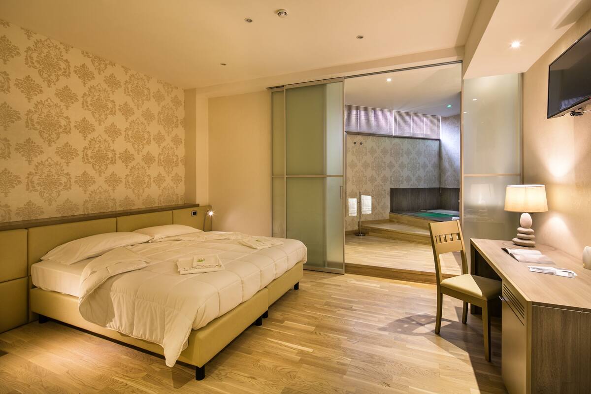 A modern hotel room with a bed, desk, chair, and a sliding door leading to a bathroom.