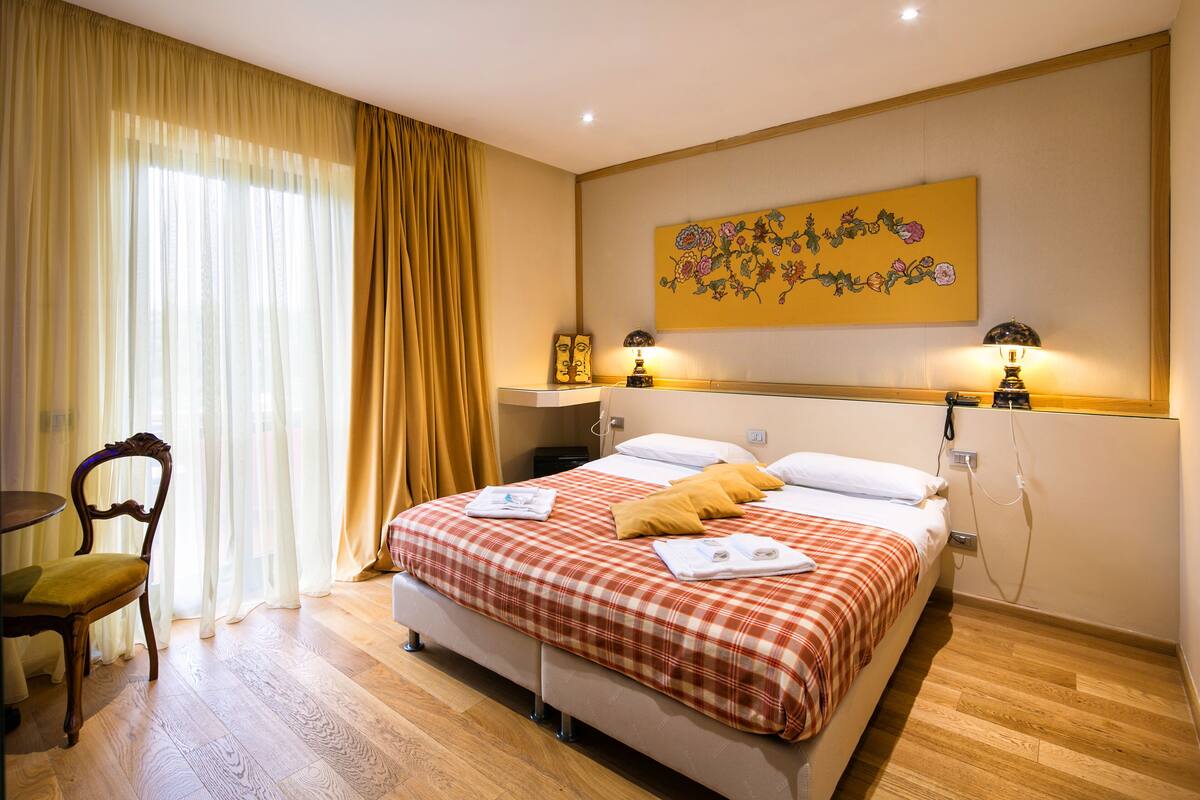 A hotel room with a bed, a chair, a table, and a painting on the wall.
