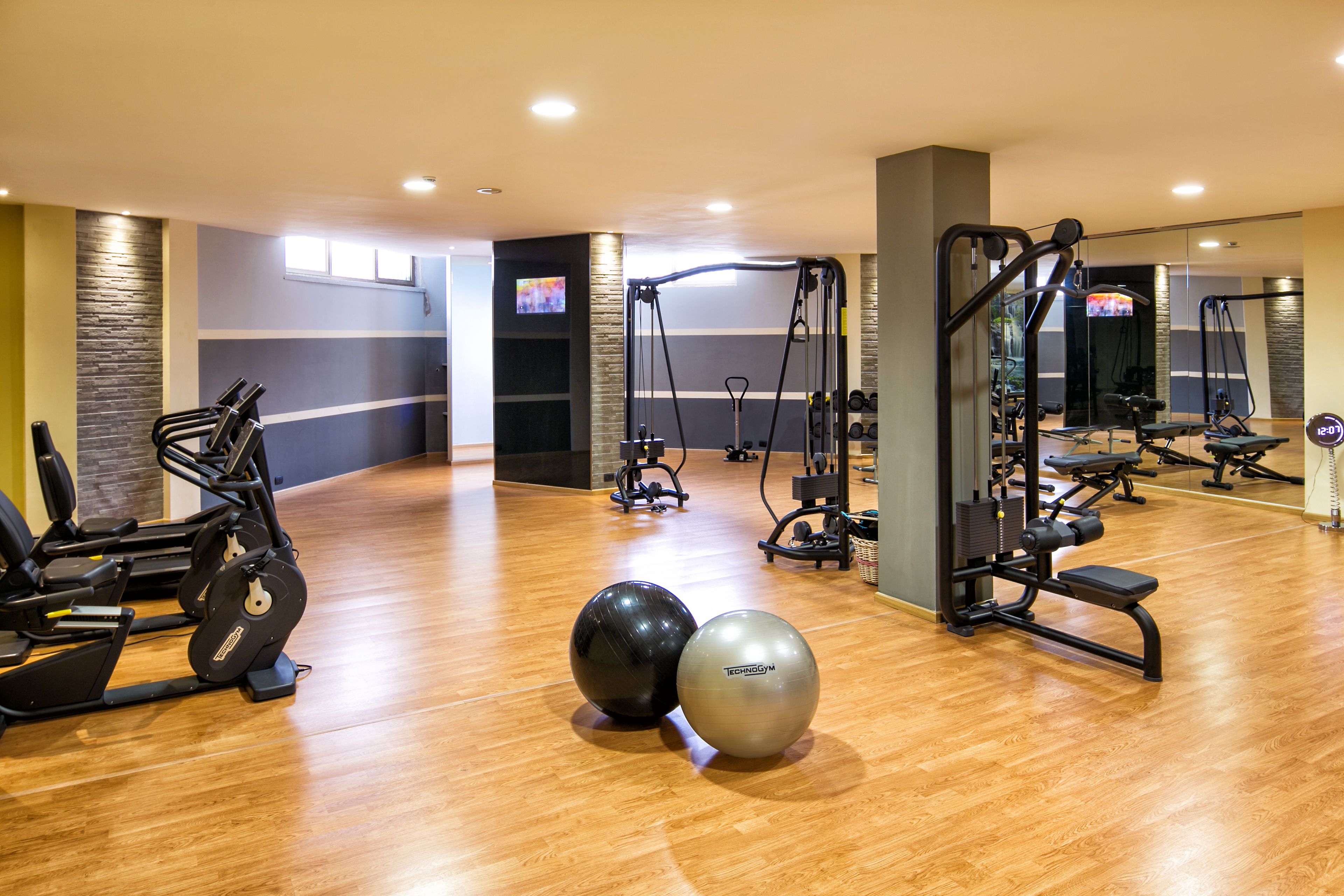 Un gimnasio con equipo de ejercicio, suelo de madera y un espejo.