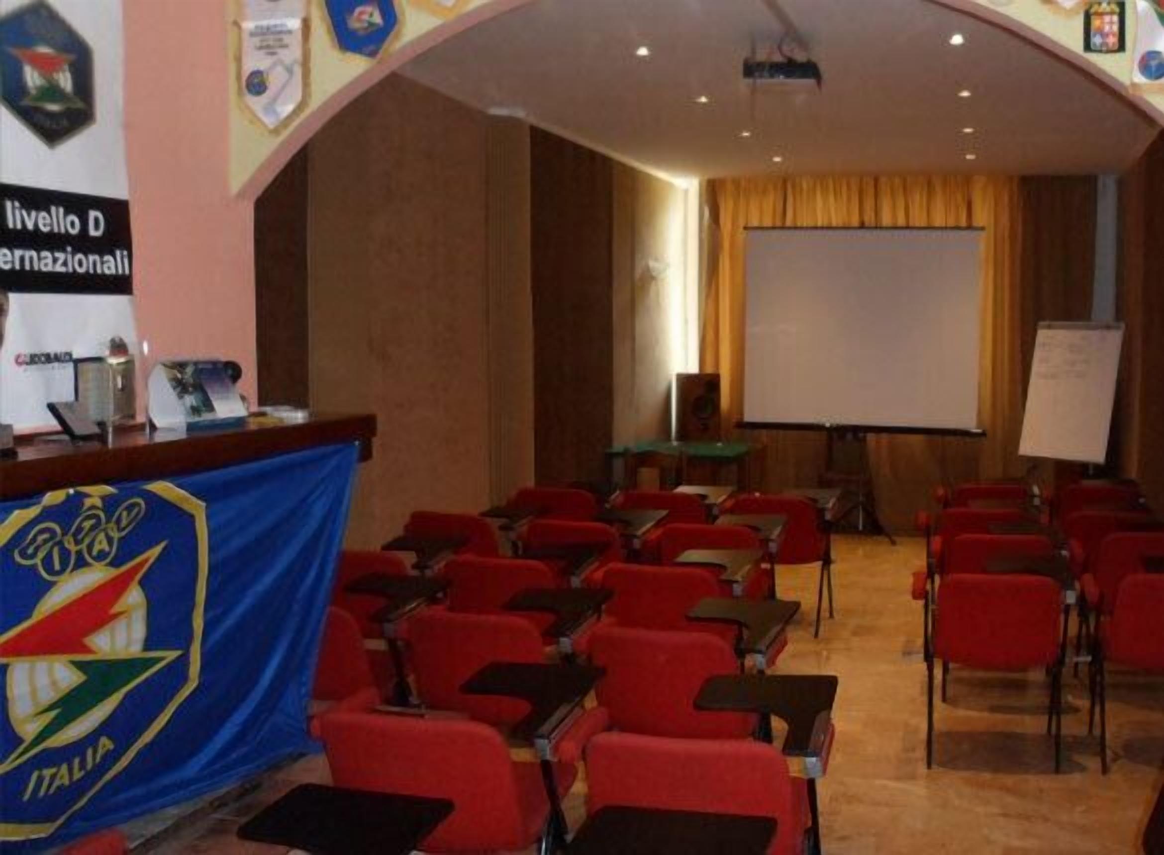 Una sala conferenze con sedie rosse, un leggio e uno schermo di proiezione.
