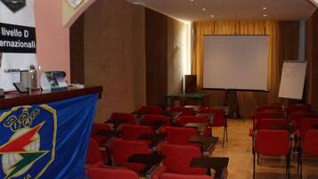 Una sala conferenze con sedie rosse, un leggio e uno schermo di proiezione.