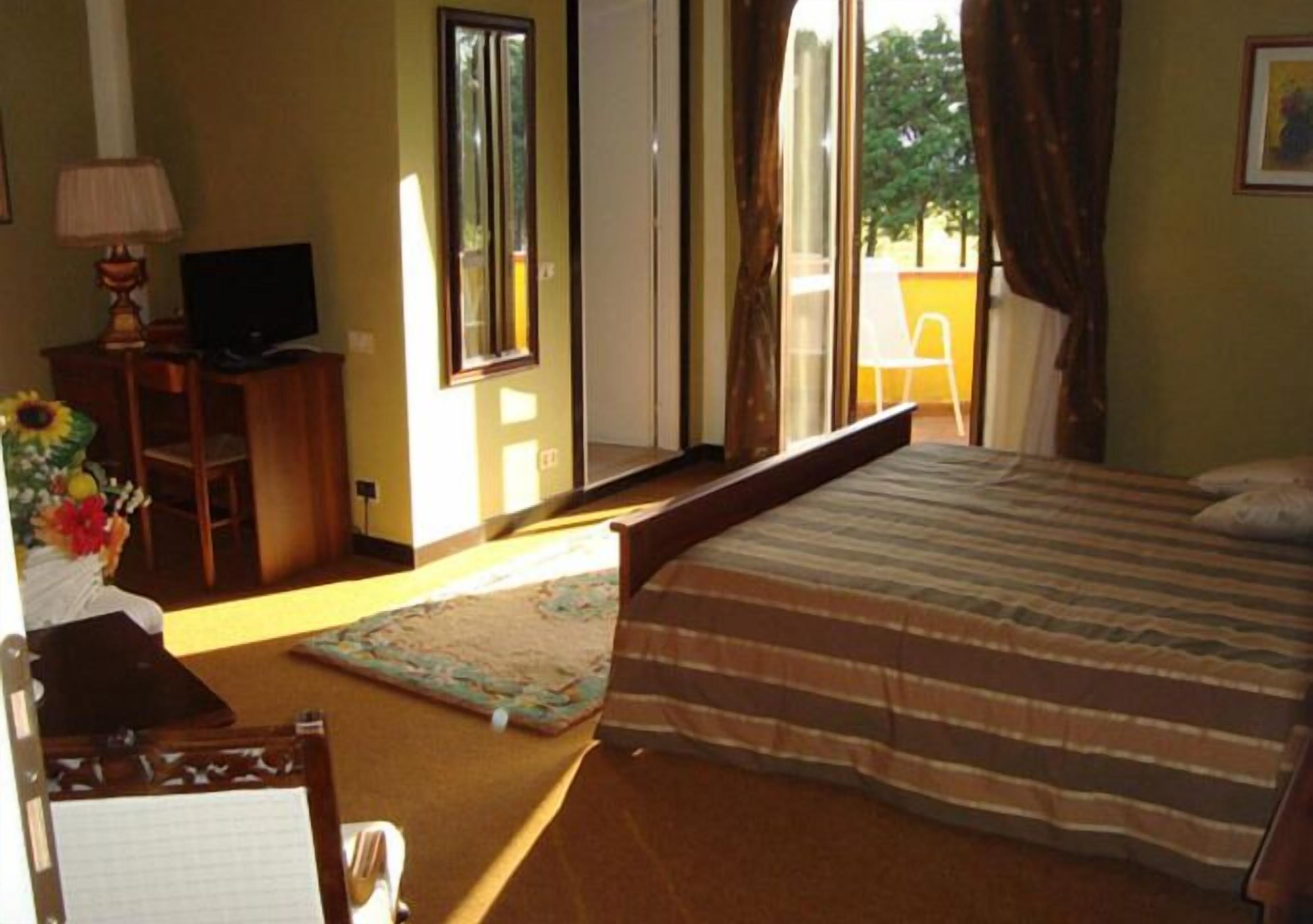 Ein Schlafzimmer mit einem Bett, einem Schreibtisch mit Computer, einem Stuhl und einem Fenster mit Vorhängen.