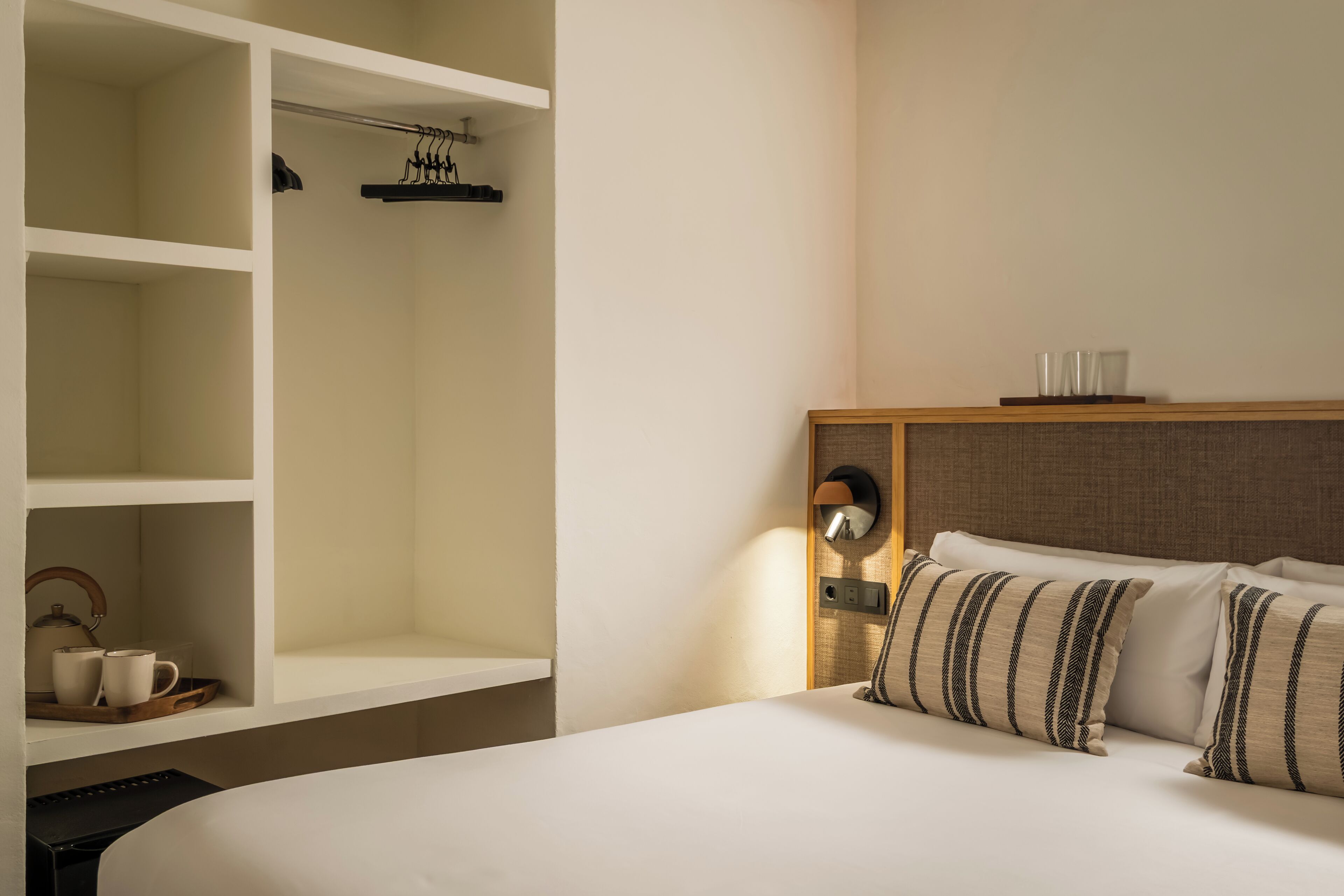 Een hotelkamer met een bed, een garderobe, een nachtkastje met een lamp, en een dienblad met kopjes en een theepot.