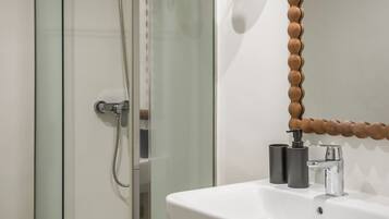 Un baño moderno con cabina de ducha de vidrio, un lavabo blanco con un espejo redondo y toallas dobladas con cuidado.