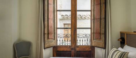 A bedroom with a bed, a chair, and a wooden door with a view to the outside.