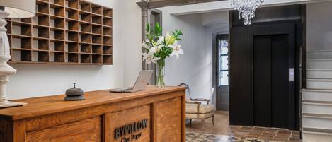A reception desk with a laptop, a vase of flowers, and a wooden panel with the text "BYPILLOW Che Bregu".