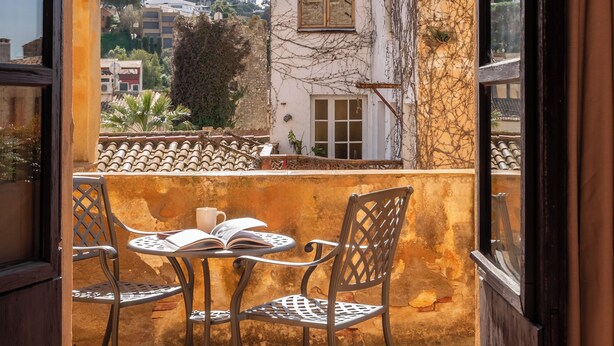 An open balcony with a table and chairs, a view of a building with vines, and a clear sky. - BYPILLOW Cluc Begur (Begur)