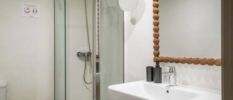 A modern bathroom with a glass-enclosed shower, a white sink, and a wooden stool.