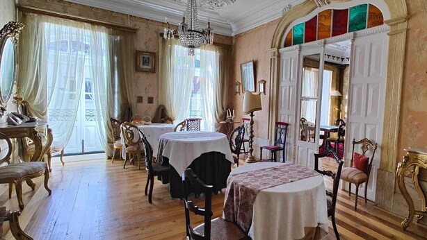 A room with a dining area featuring round tables and chairs, a chandelier, and a large mirror with framed pictures.