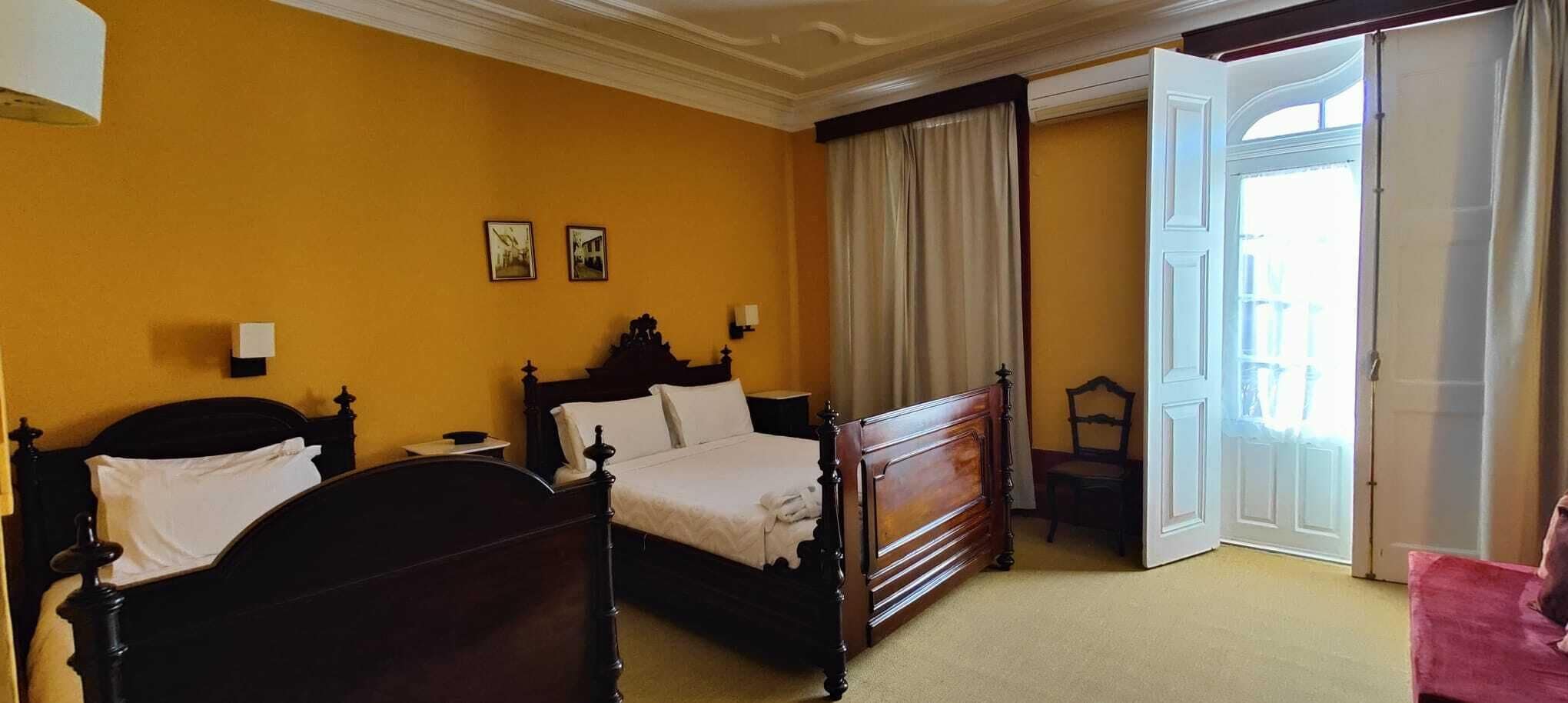 A hotel room with two wooden beds, a chair, a nightstand, and a window with curtains.