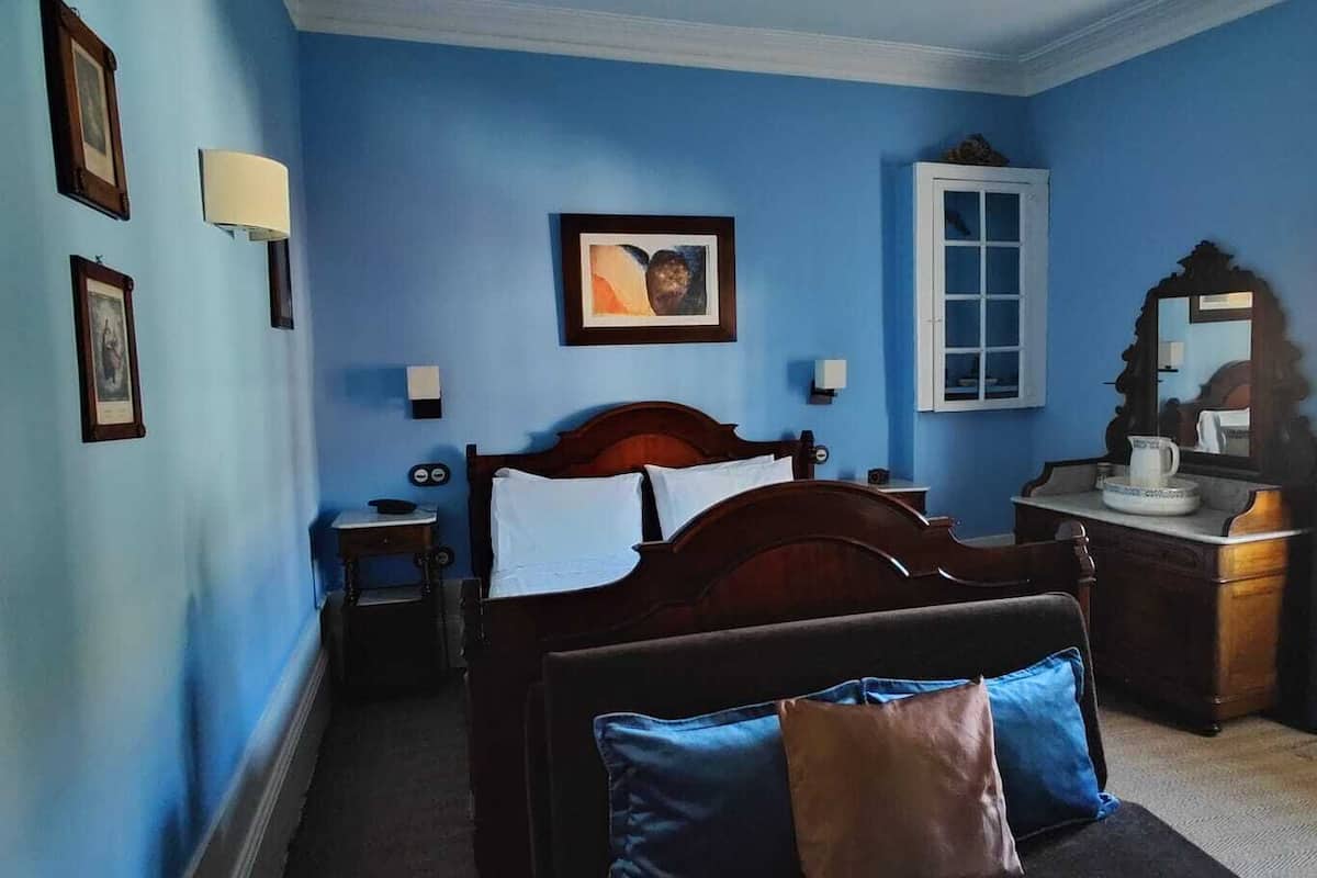 A bedroom with a bed, bedside table, dresser, and a window with curtains.