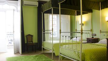 A four-poster bed with green bedding, a wooden chair, and a nightstand with a lamp.