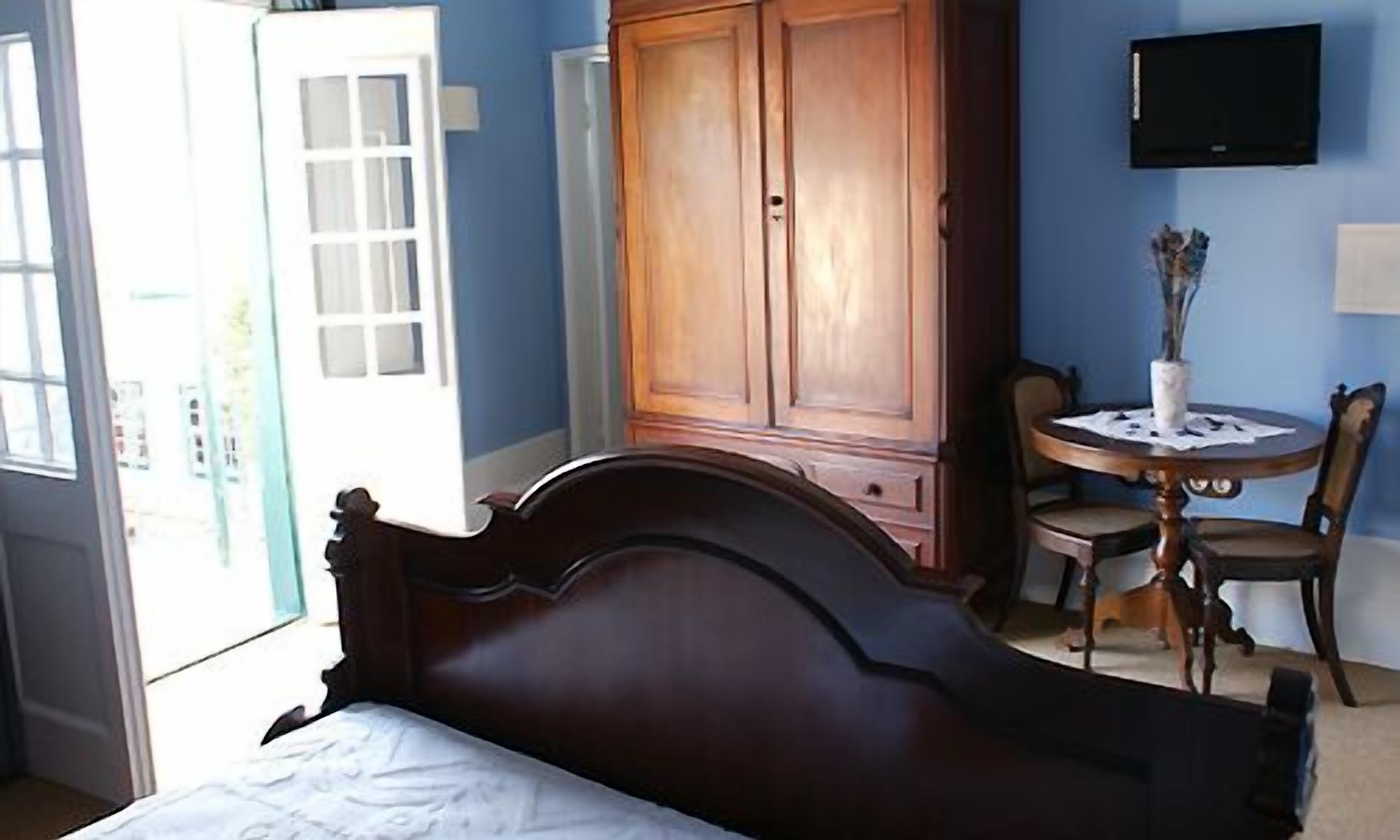 A bedroom with a wooden bed, a wardrobe, a TV mounted on the wall, and a small round table with chairs.