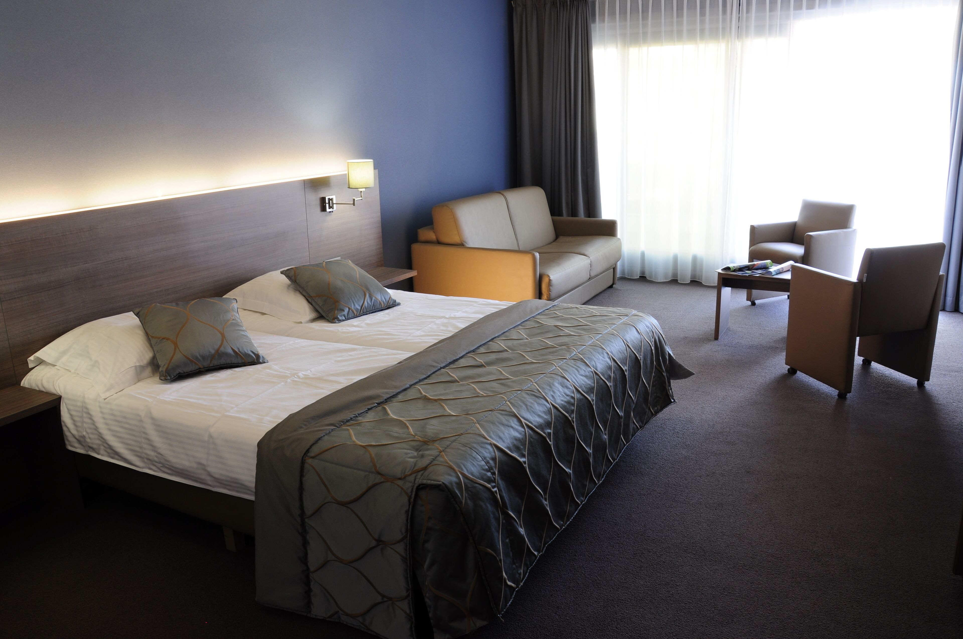 A hotel room with a large bed, a sofa, a chair, and a small table.