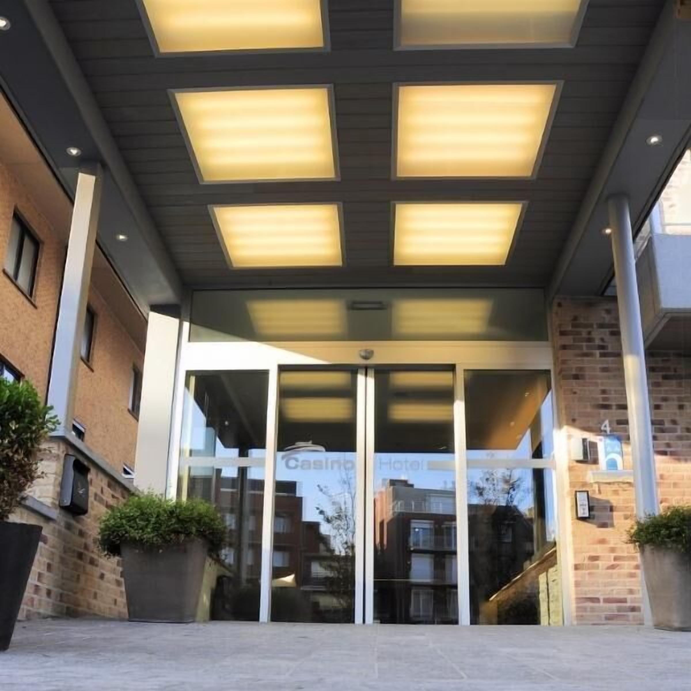L’entrée d’un hôtel au design moderne, avec une porte en verre portant une enseigne, une façade en briques et un toit plat agrémenté de lucarnes.