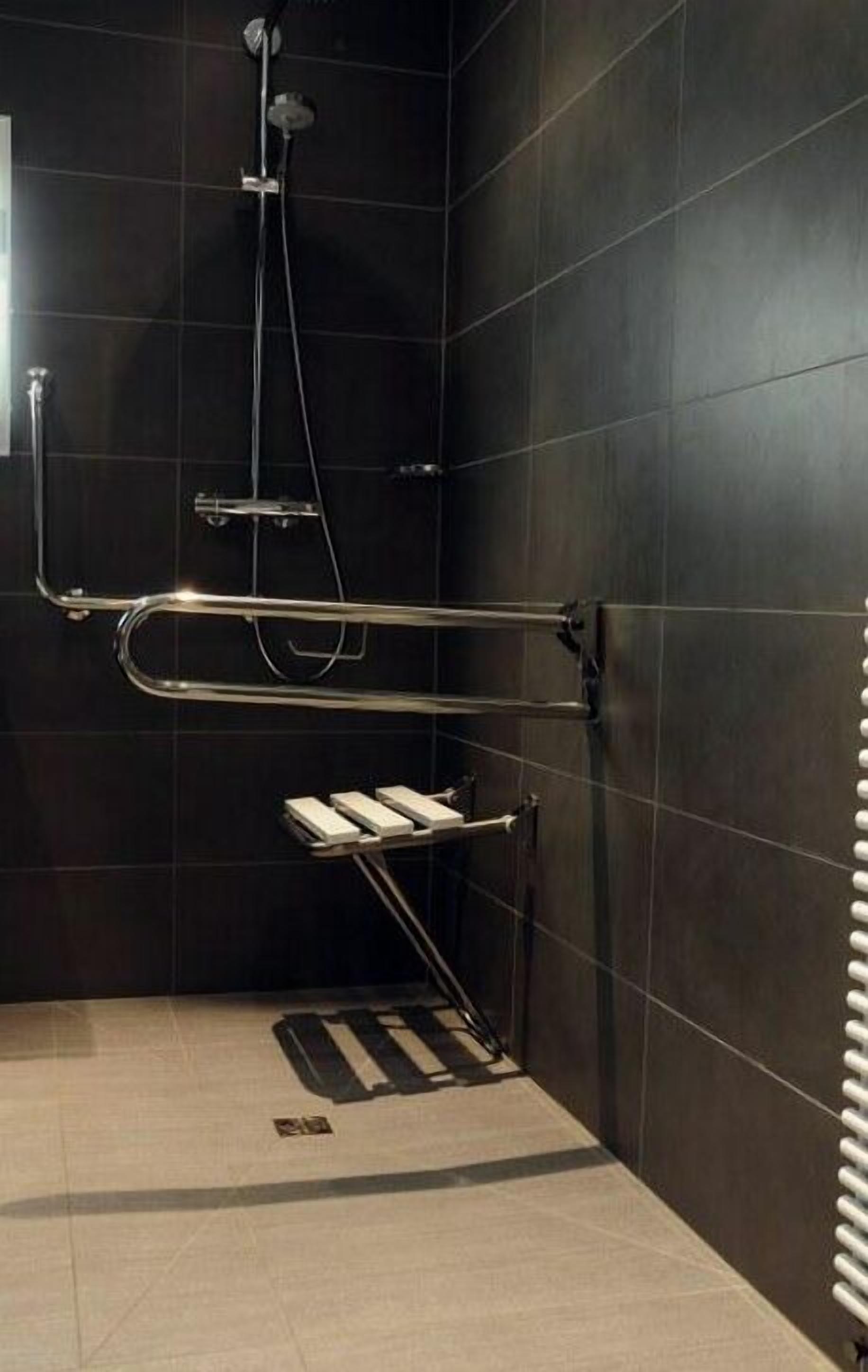 A modern bathroom with dark tiled walls, a glass shower enclosure, and a metal towel rack.