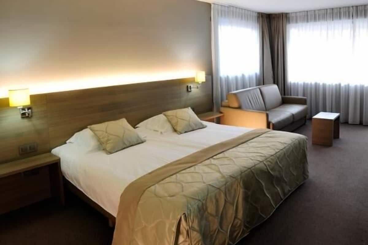 A hotel room with a large bed, a sofa, a nightstand, and a lamp.