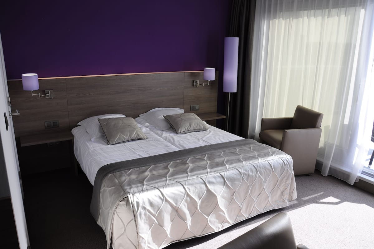 A hotel room with a bed, two bedside tables, a chair, and a window with curtains.