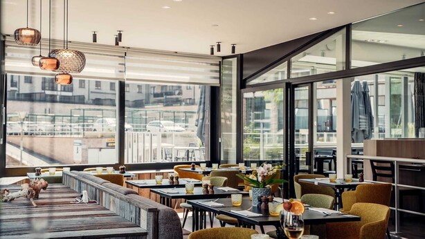 A modern restaurant with high ceilings, large windows, and a variety of seating options including tables and benches. - Casino Hotel (Koksijde)