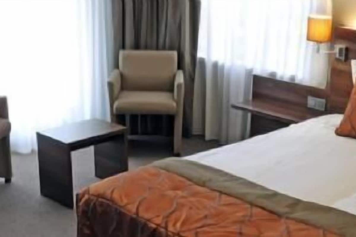 A hotel room with a bed, a chair, a small table, and a nightstand.