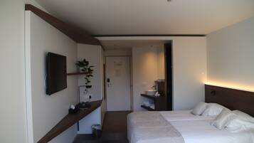 A hotel room with two beds, a TV mounted on the wall, a small plant, and a bedside table.