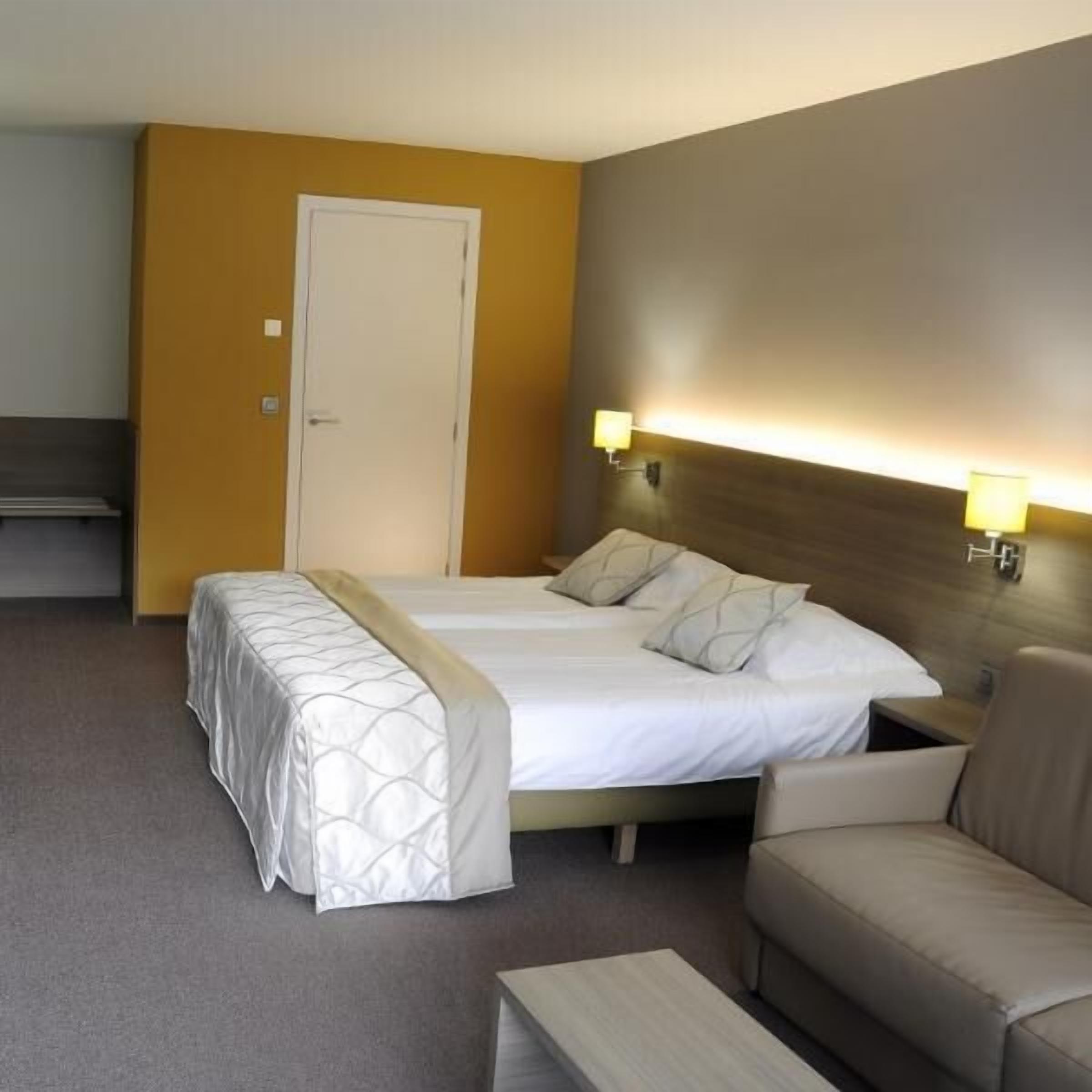 Een hotelkamer met een bed, twee bedlampen, een bank en een kleine tafel.