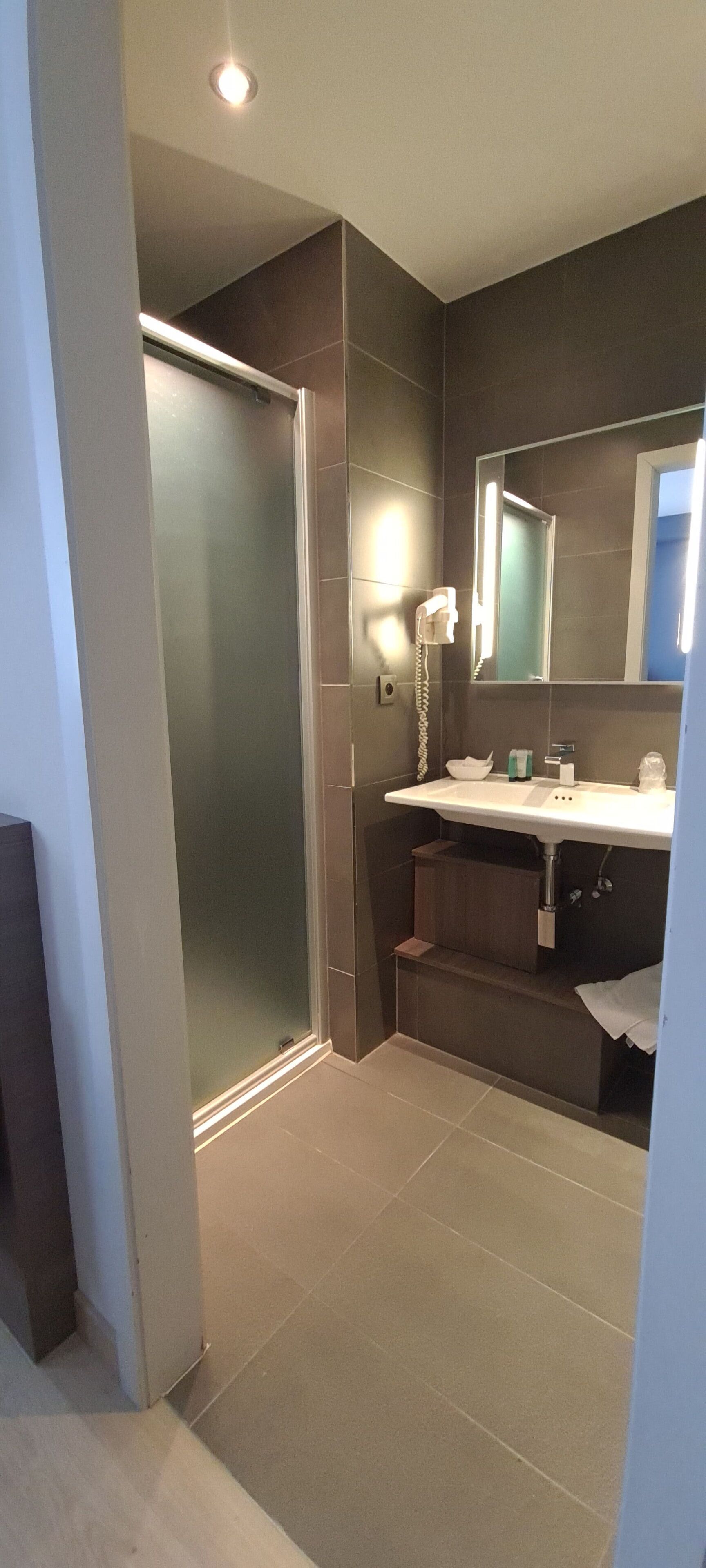 A modern bathroom with a glass shower door, a sink with a mirror, and a hairdryer on the wall.