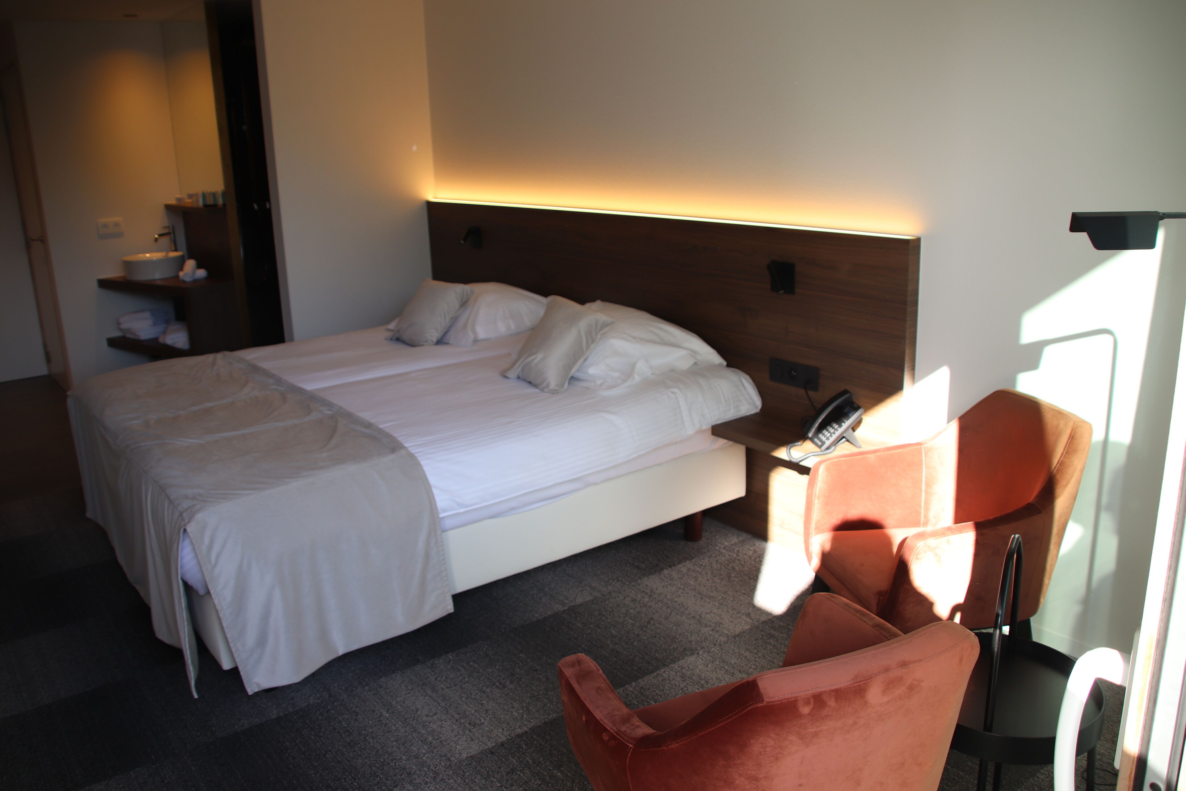 Et hotelværelse med en dobbeltseng, et natbord med lampe, en stol og et lille bord med telefon.