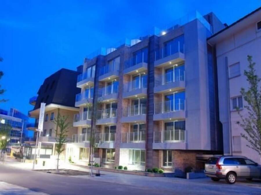A multi-story hotel with balconies, a parking area, and a street view.