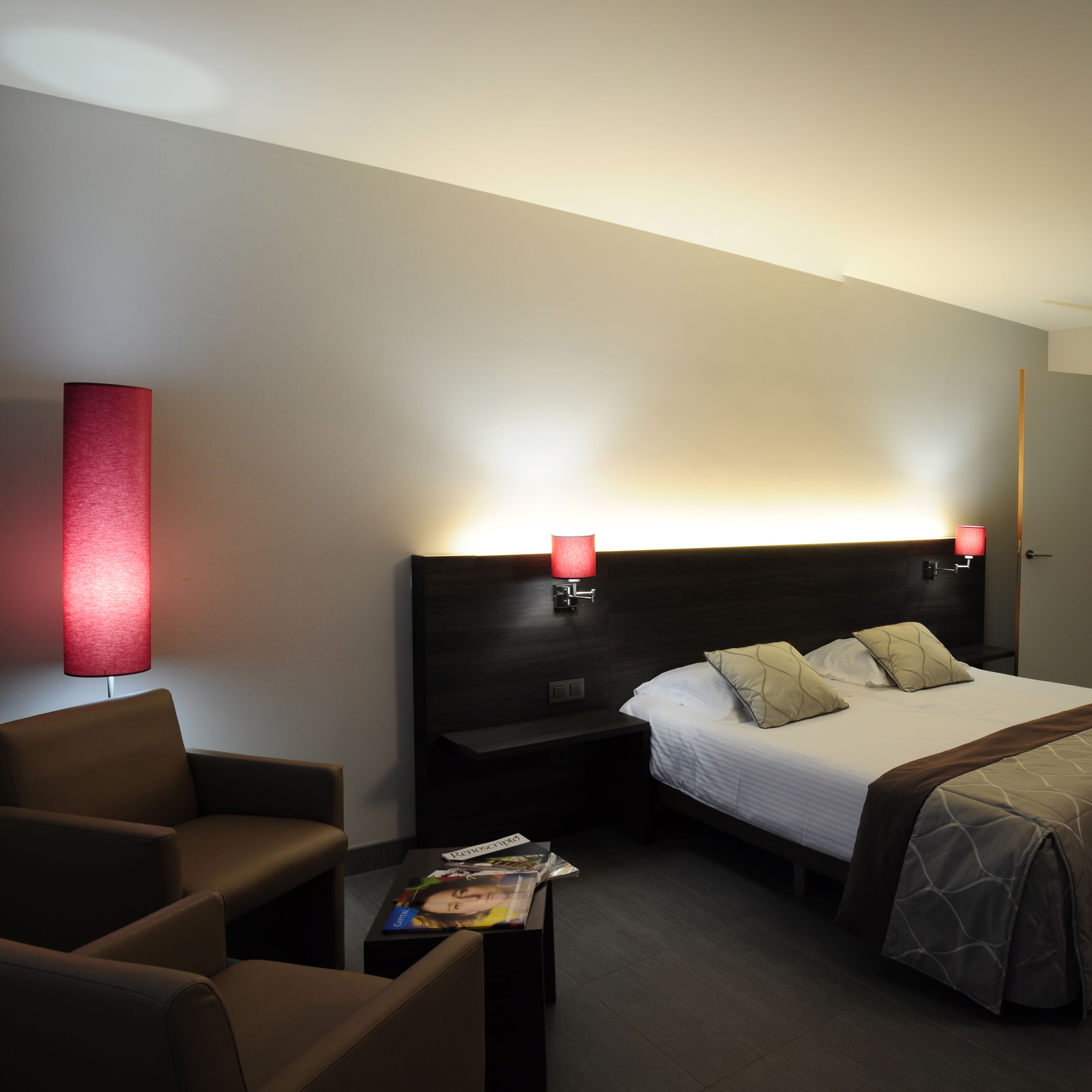 Une chambre d’hôtel avec un lit, deux lampes de chevet, une table de chevet, une chaise et un magazine sur la table de chevet.
