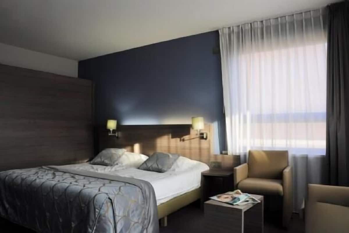 A modern hotel room with a large bed, two bedside lamps, a small table, and a chair.