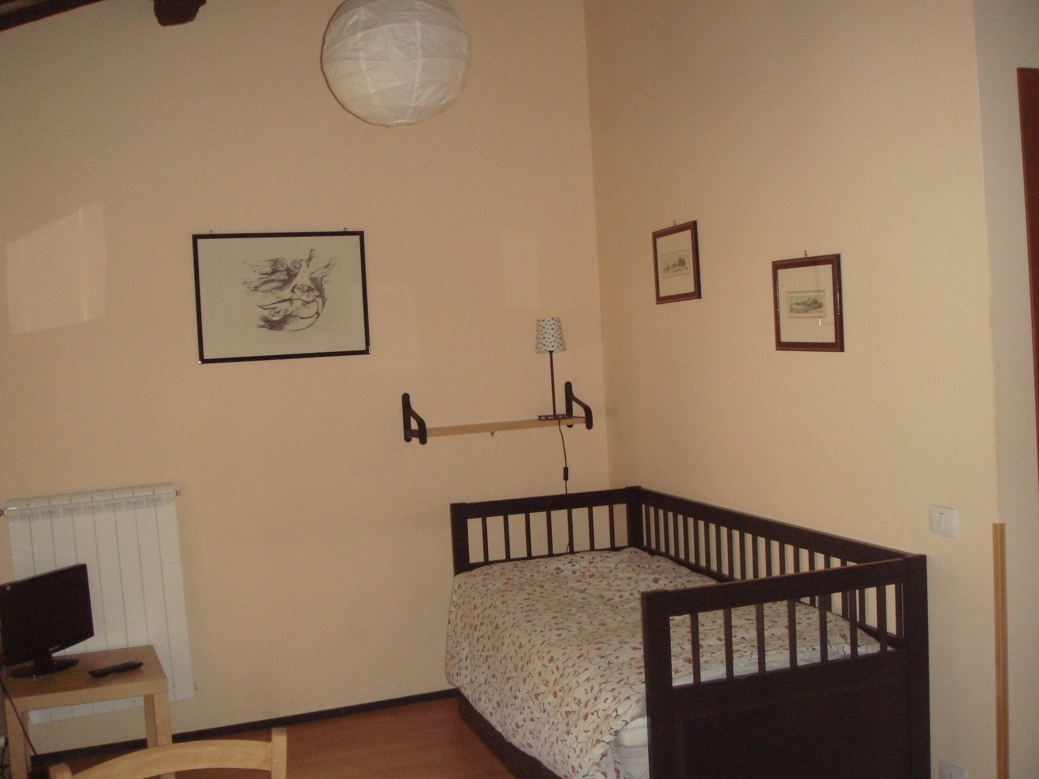 A small, well-lit room with a crib, a desk with a computer, and a radiator.