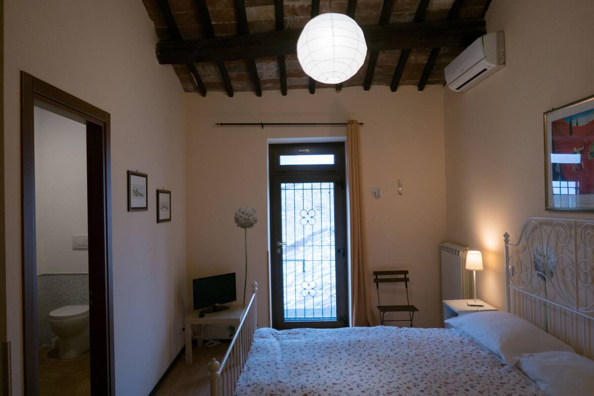 Une chambre à coucher avec un lit, un bureau, une chaise, un téléviseur et une fenêtre avec des rideaux.