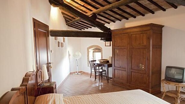 Quarto com teto de madeira, uma cama, guarda-roupa de madeira, escrivaninha com cadeira e televisão.