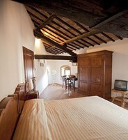 A bedroom with a wooden ceiling, a bed, a wooden wardrobe, a desk with a chair, and a television.