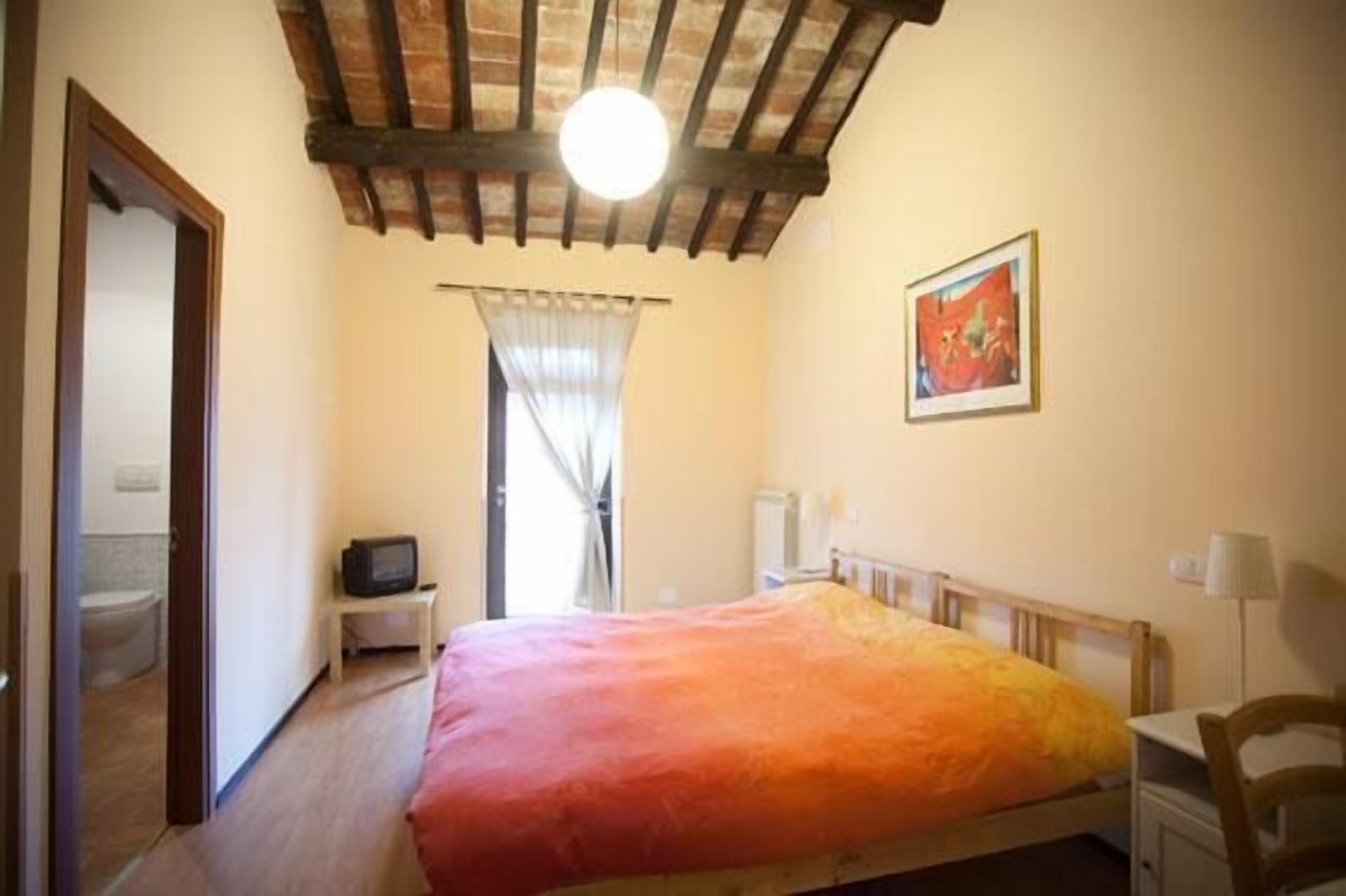 A bedroom with a bed, a television, a window with curtains, a radiator, and a painting on the wall.