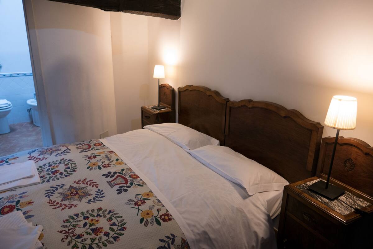 Un lit bien fait, avec une couvre-lit à motifs floraux, une tête de lit en bois et deux lampes de chevet.