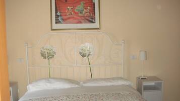 Un dormitorio con cama, mesita de noche, lámpara y un cuadro en la pared.